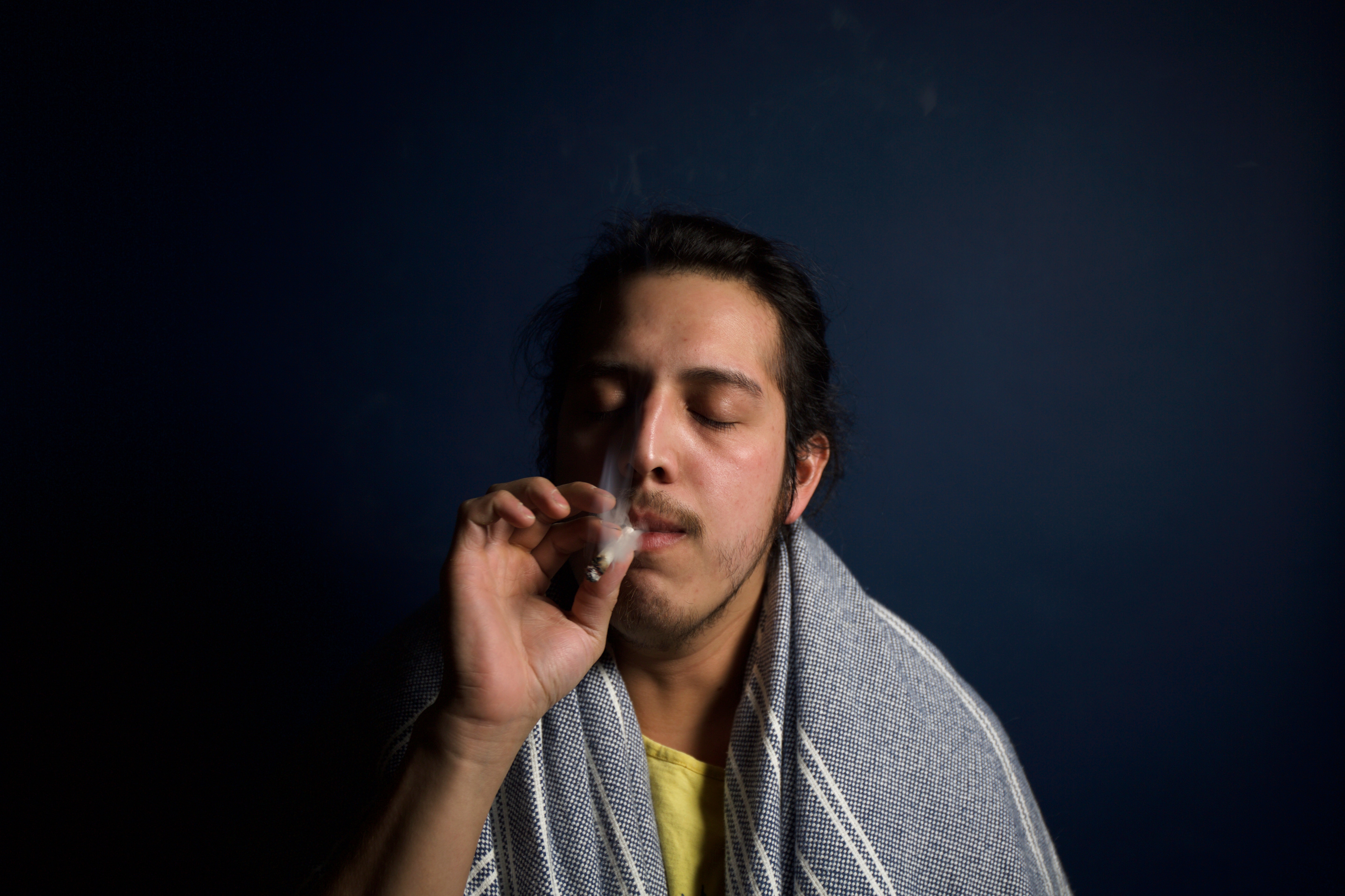 A millenial young man wearing a scarf on his shoulder deeply immersed in his smoking of cannabis.